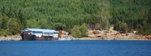 A logging operation on the shoreline along Cordero Channel.  These are usually temporary camps, set up while they're logging in the nearby backwoods.  When we first spotted the large vessel hull, we thought it might be a grounded freighter, with buildings behind it on the shore.  With the binoculars we could tell it's a clever "camp" they can tow from site to site, utilizing an old ship's hull with office and housing quarters built atop it.  All of the heavy equipment on shore is most likely brought in on a barge.